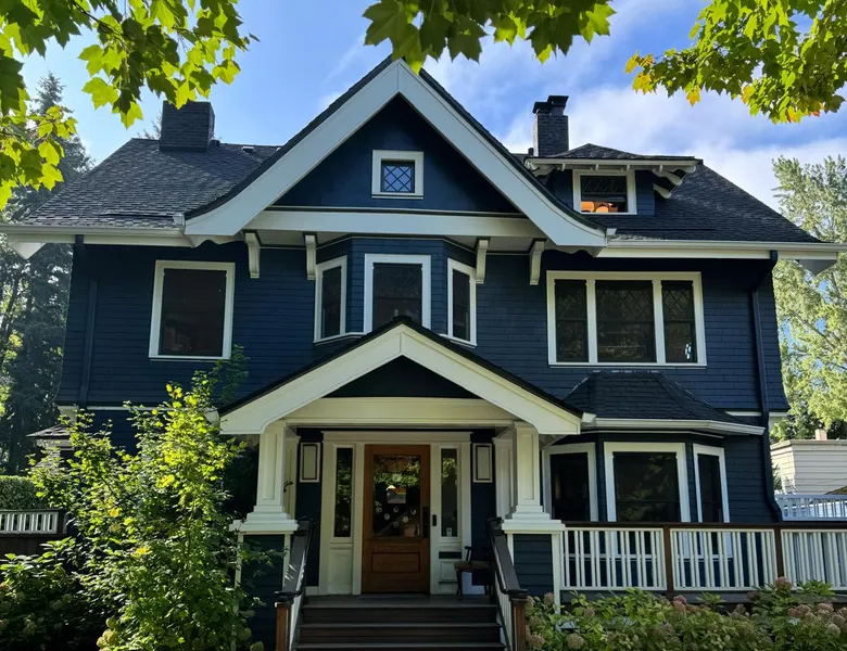 Craftsman house painted navy blue with crisp white trim, porch columns and brackets, an exterior painted by Olvera Painting