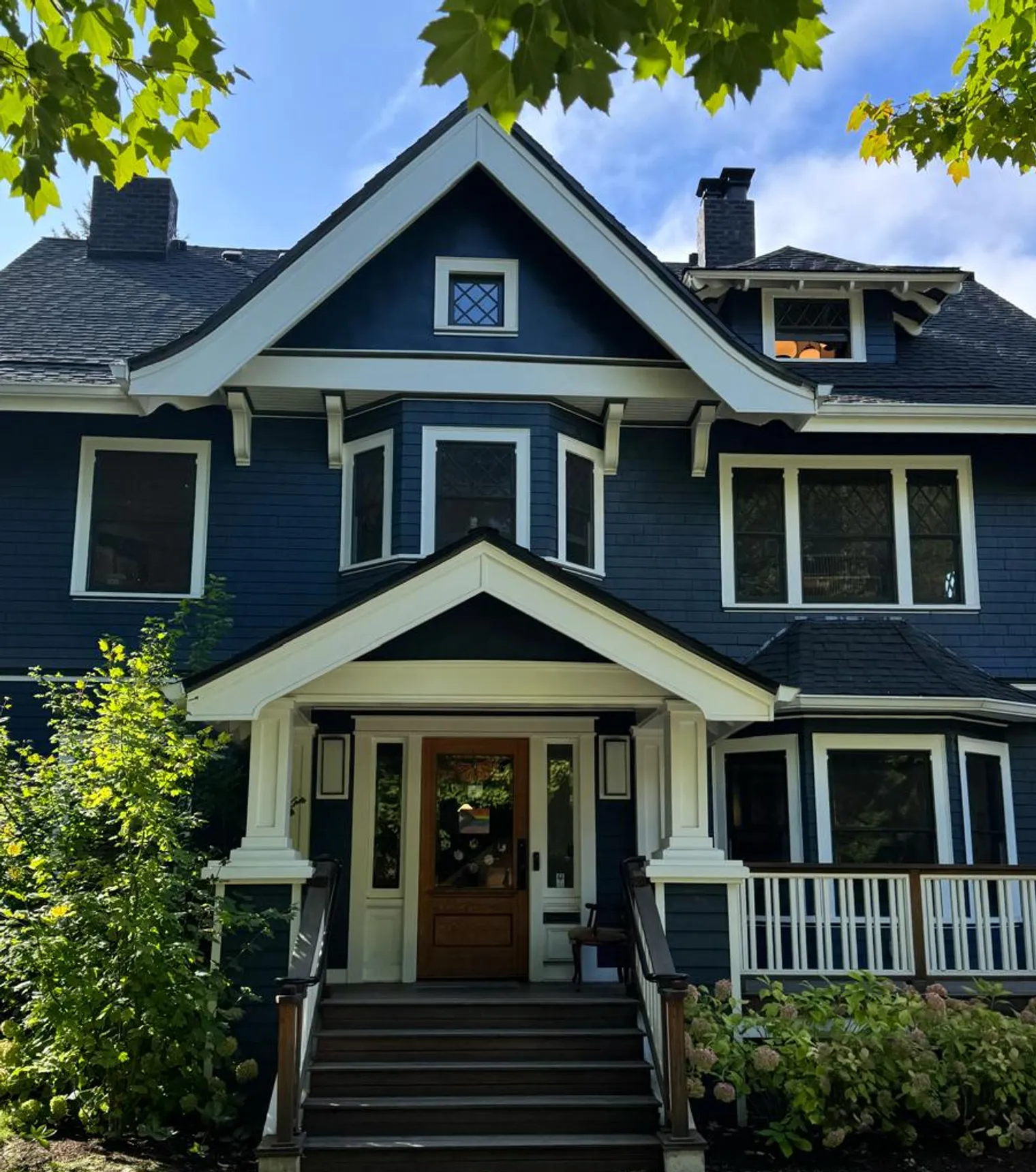 Craftsman house painted navy blue with crisp white trim, porch columns and brackets, an exterior painted by Olvera Painting
