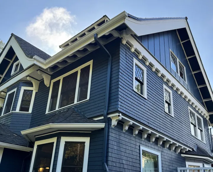 Side of a craftsman house painted navy with white brackets, window trim and deck railing