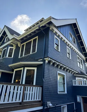 Side of a craftsman house painted navy with white brackets, window trim and deck railing