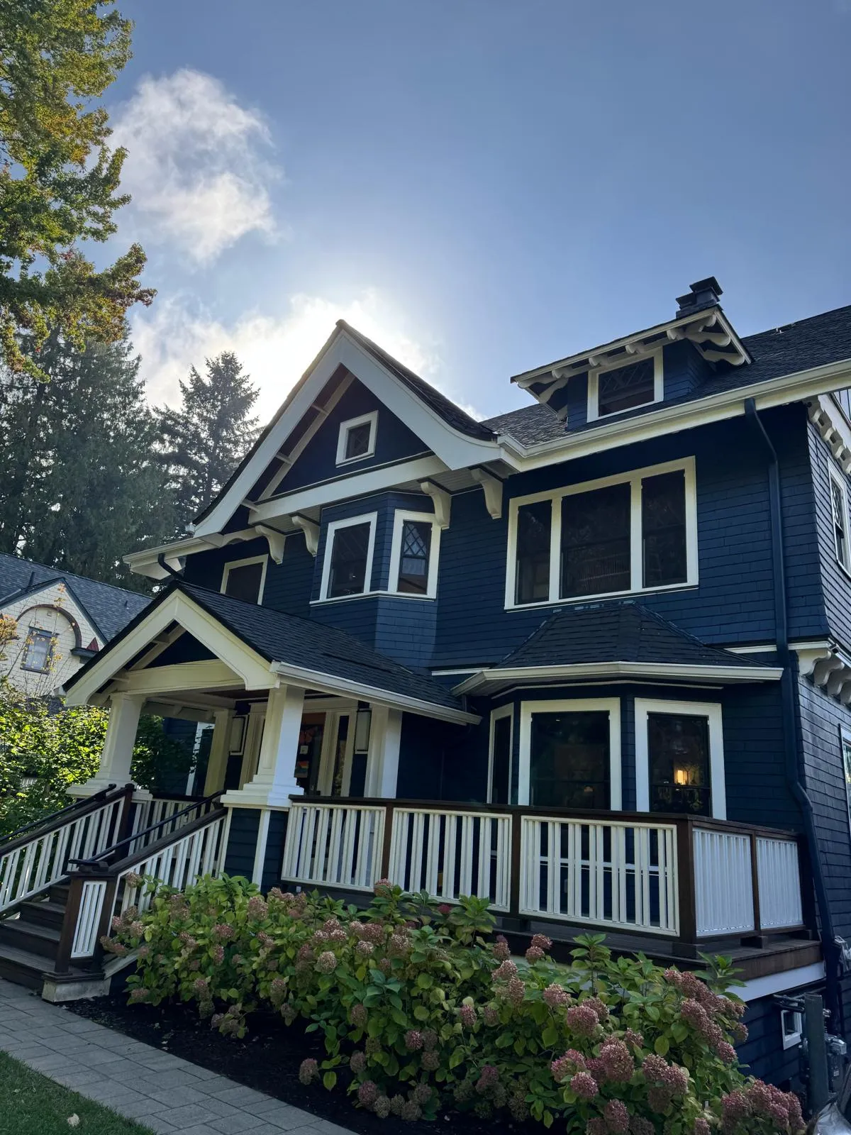 Craftsman porch with white columns and railing against navy shingle siding