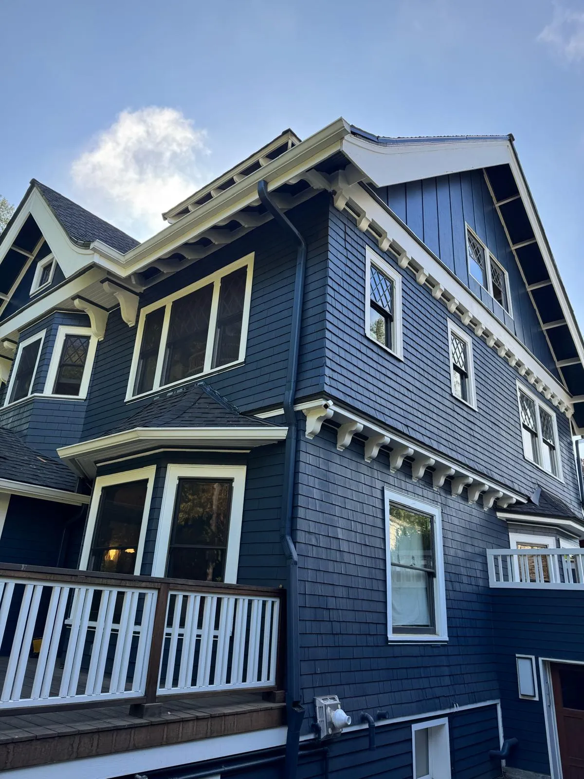 Side of a navy shingle house with rows of white brackets and white window trim