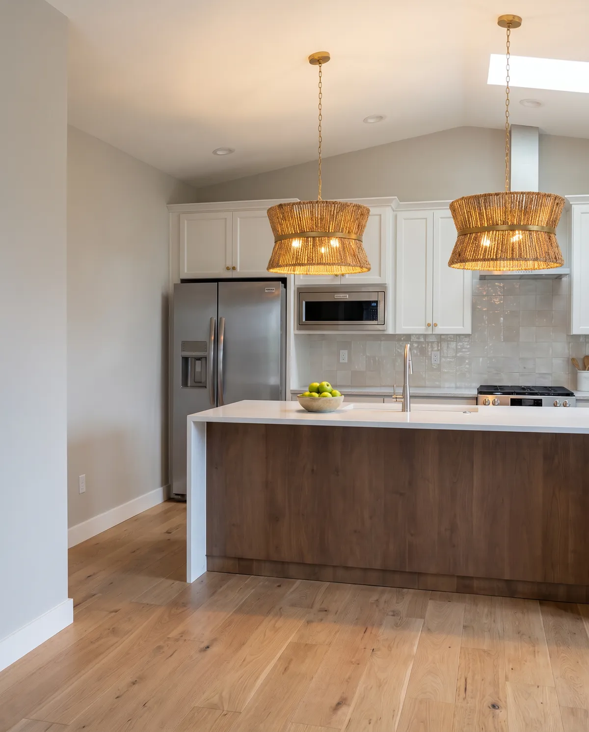 Finished kitchen with white walls, white cabinets, rattan pendant lights and a walnut island