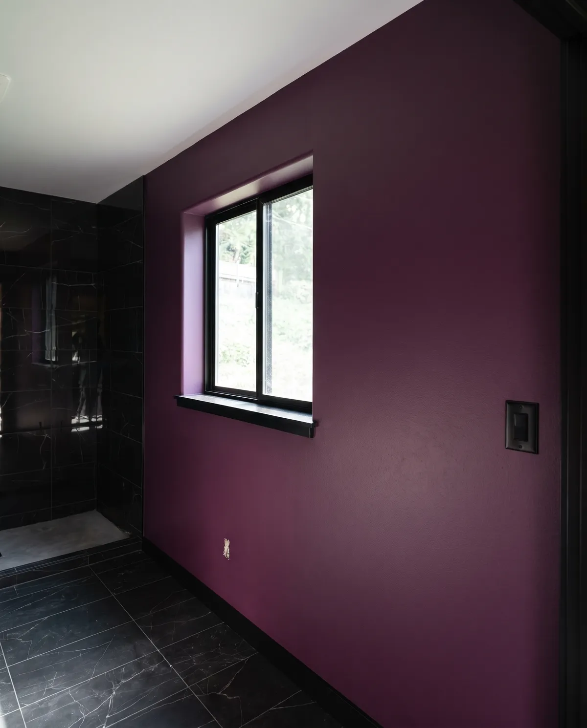 Plum accent wall around a black-framed window in a bathroom with dark tile