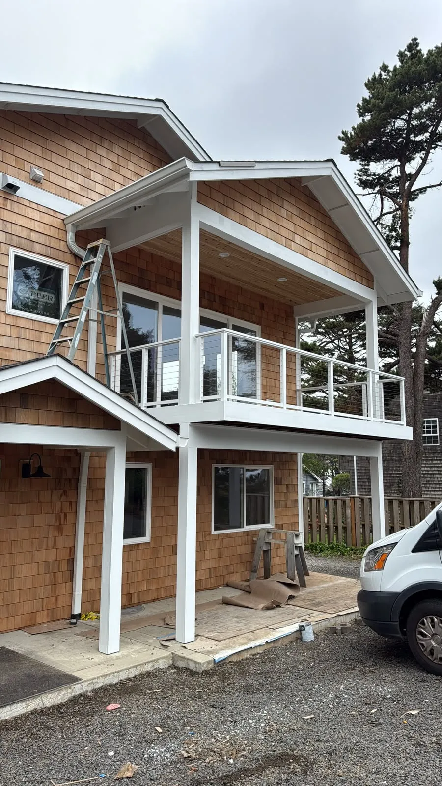 Two-story cedar-shake house with white trim and a balcony during an Olvera Painting exterior job, a ladder against the wall