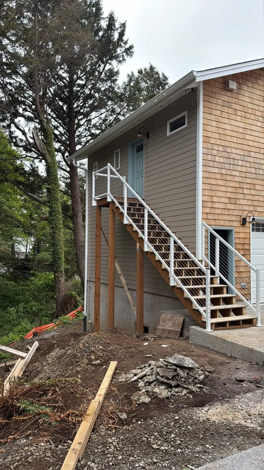Cedar shake and lap siding house with white exterior stairs, site work still in progress