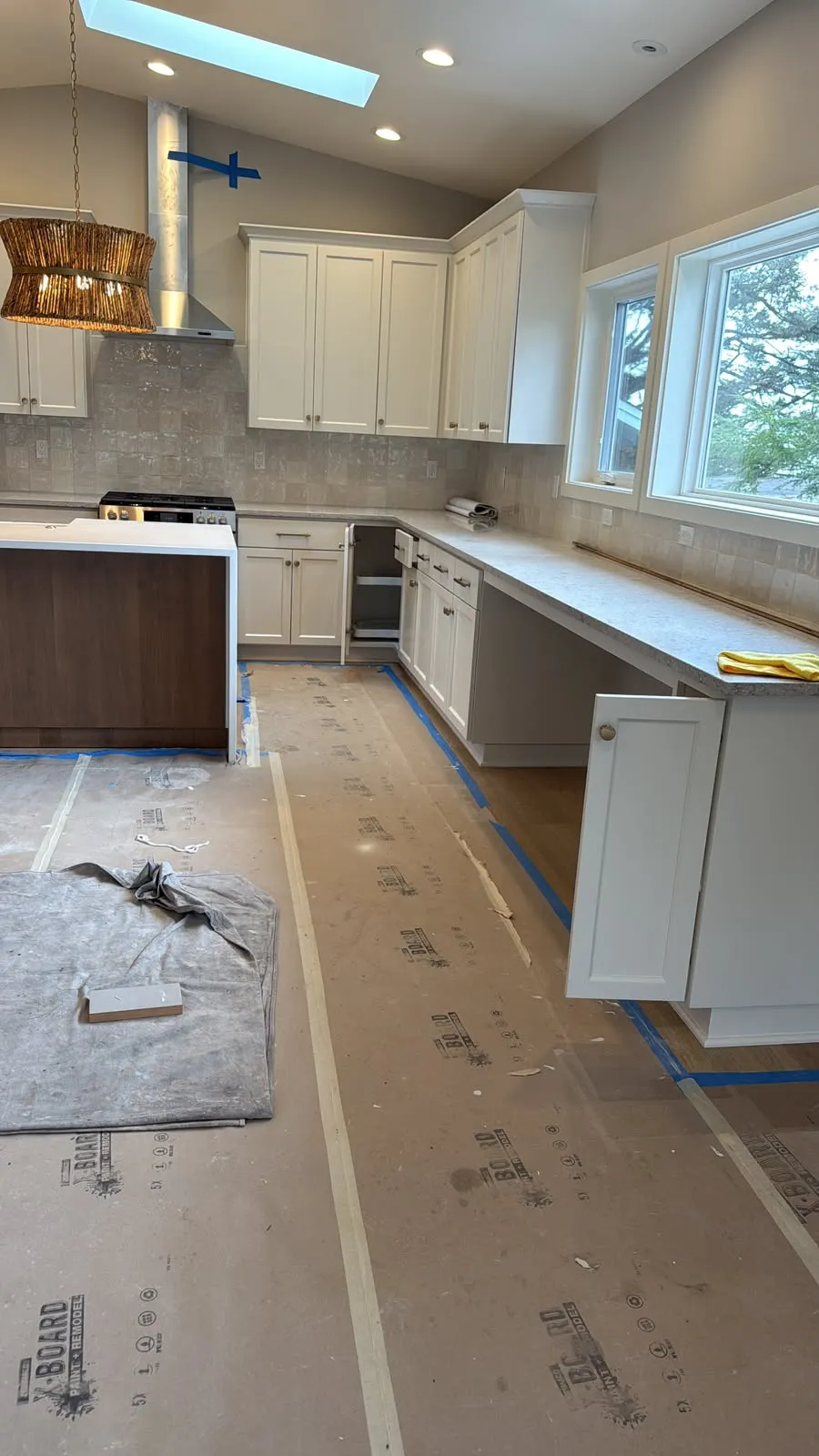 Kitchen with white shaker cabinets and the floor covered with protective paper and blue tape